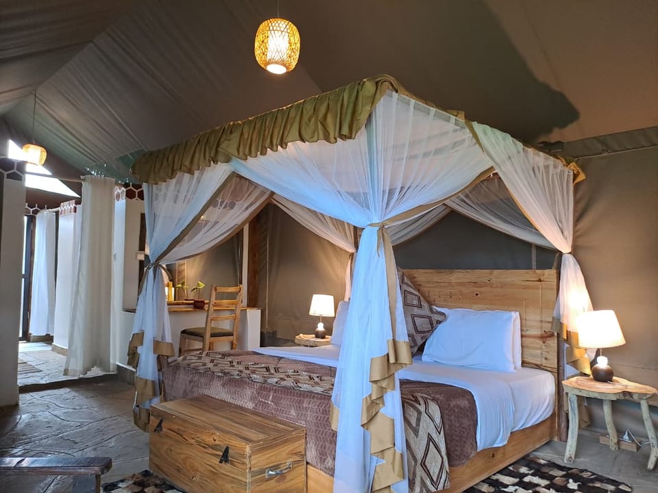 Canopied four-poster bed with white mosquito net and carved wooden headboard inside a tented suite