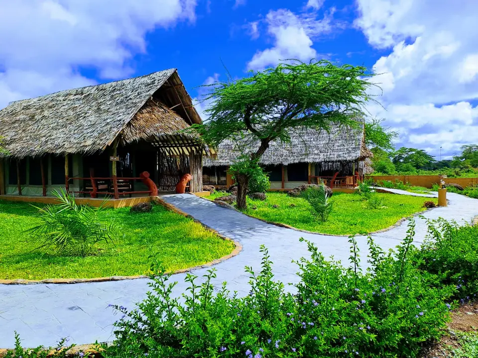Thatched tented suites with verandas behind a lawn and a flowering hedge